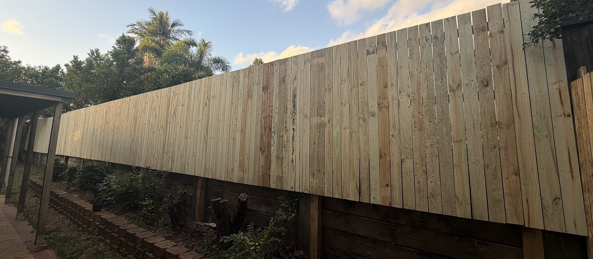 A finished timber paling fence running the full length of a back boundary above a sleeper retaining wall